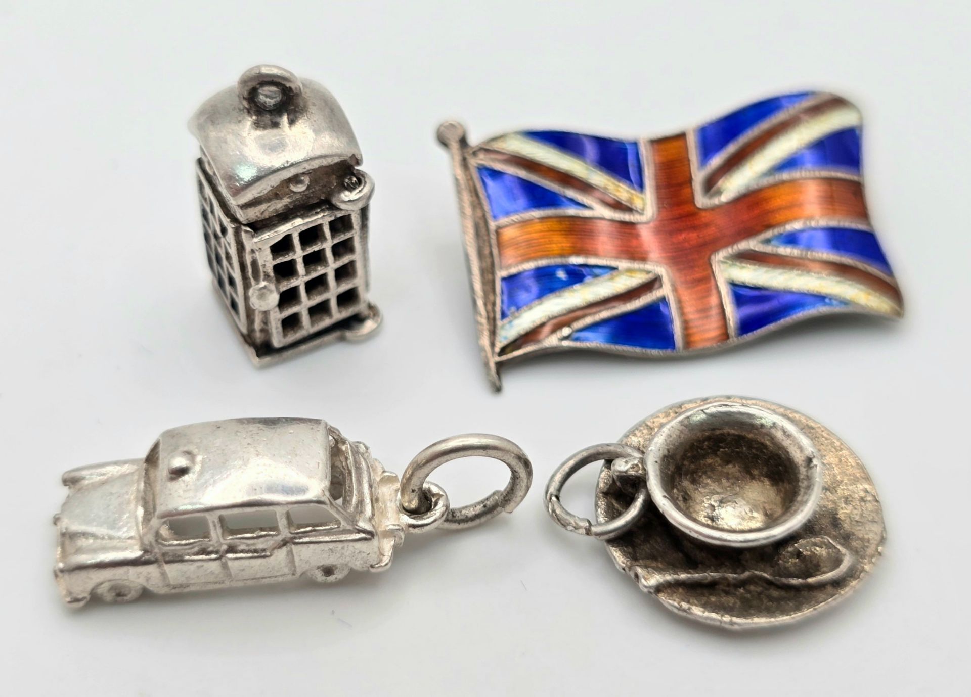 A STERLING SILVER LONDON THEMED COLLECTION OF ITEMS - UNION JACK FLAG BROOCH, CUP OF TEA CHARM,