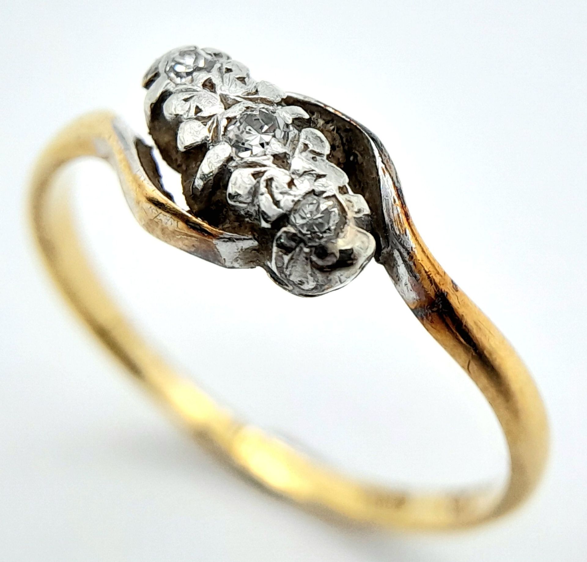 A vintage, 18 K yellow gold ring with a trilogy of round cut diamonds in a twisted design. Ring