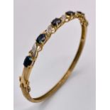 A Vintage 9K Yellow Gold Sapphire and Diamond Bangle. Six oval cut sapphires with diagonal