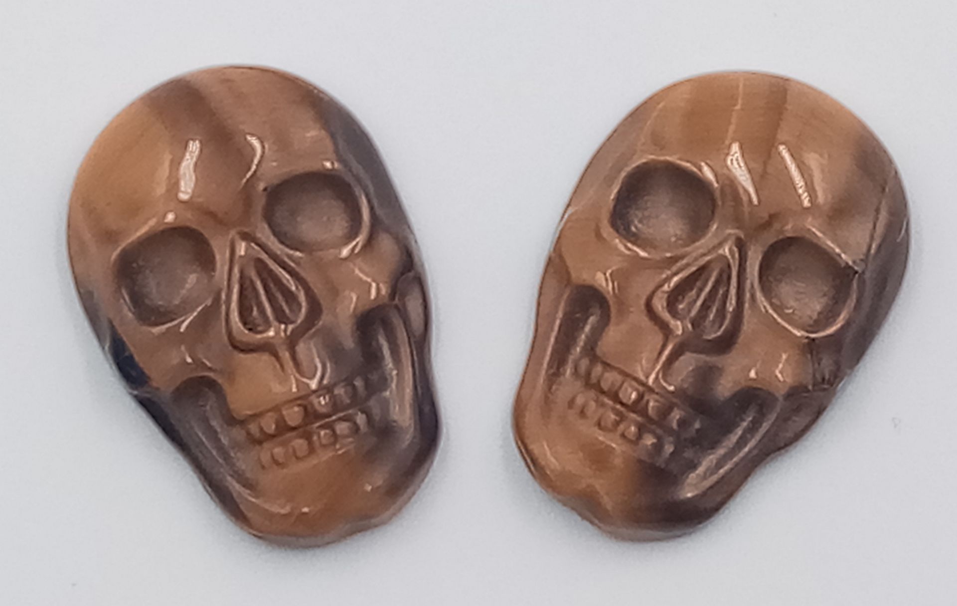 A PAIR OF TIGERS EYE CARVED MATCHING SKULLS - VERY RARE AND UNUSUAL. 20MM X 15.5MM