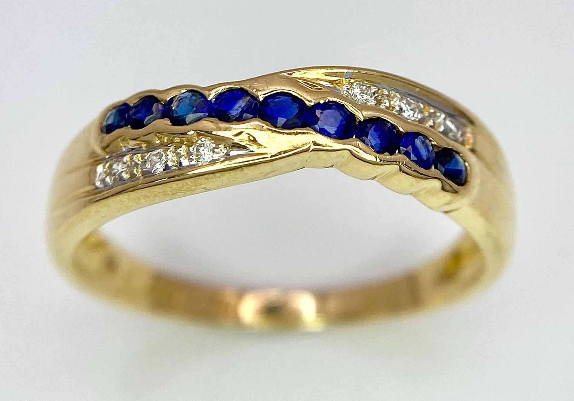 AN 18K YELLOW GOLD DIAMOND & BLUE STONE (PROBABLY SAPPHIRE) CROSSOVER RING. Size O, 2.7g total - Image 2 of 6