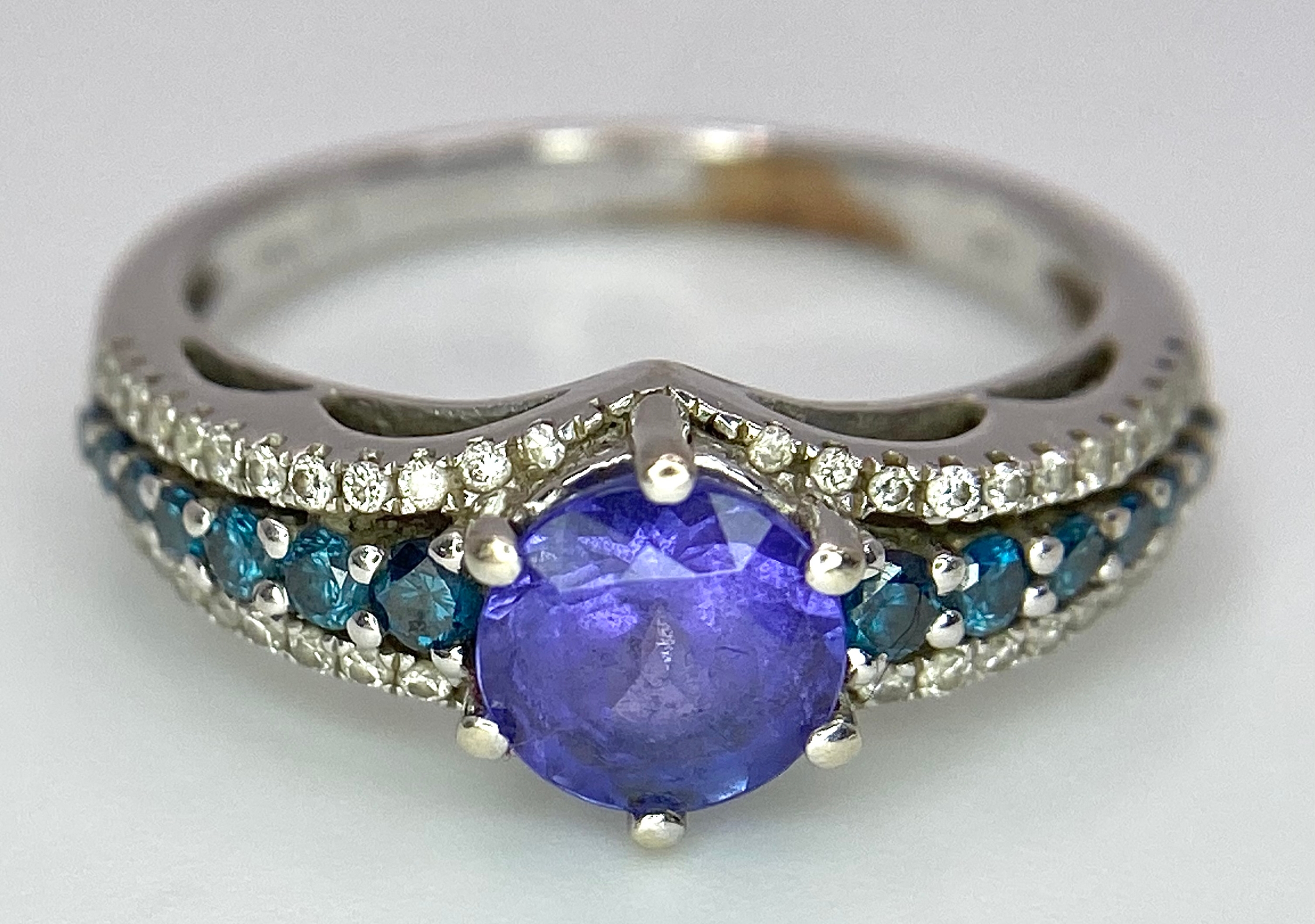 A 14K White Gold Tanzanite and Diamond Ring. Central oval cut tanzanite with blue and white diamonds