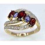 A 9 Carat Yellow Gold Garnet, Tanzanite and Diamond Set Crossover Ring Size P. Crown Measures 1.