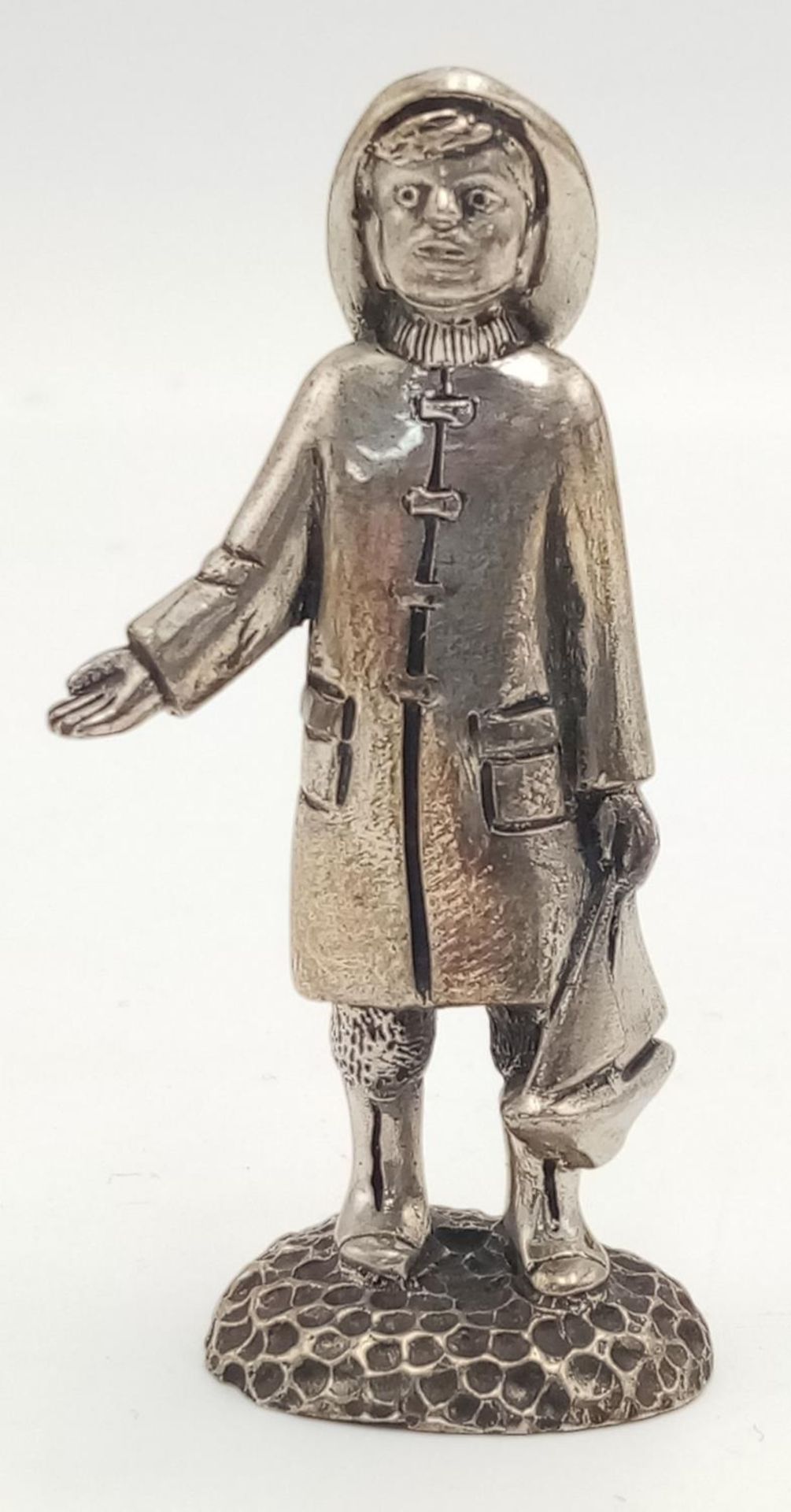 A STERLING SILVER (TESTED AS) FIGURE OF A YOUNG BOY IN RAIN JACKET AND HAT WITH A BOAT POSSIBLY