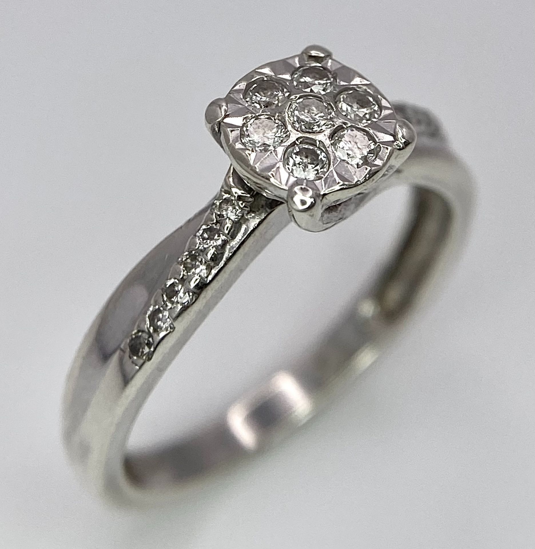 A 9K White Gold Diamond Cluster Ring. Seven small diamonds on a circular base with diamonds on