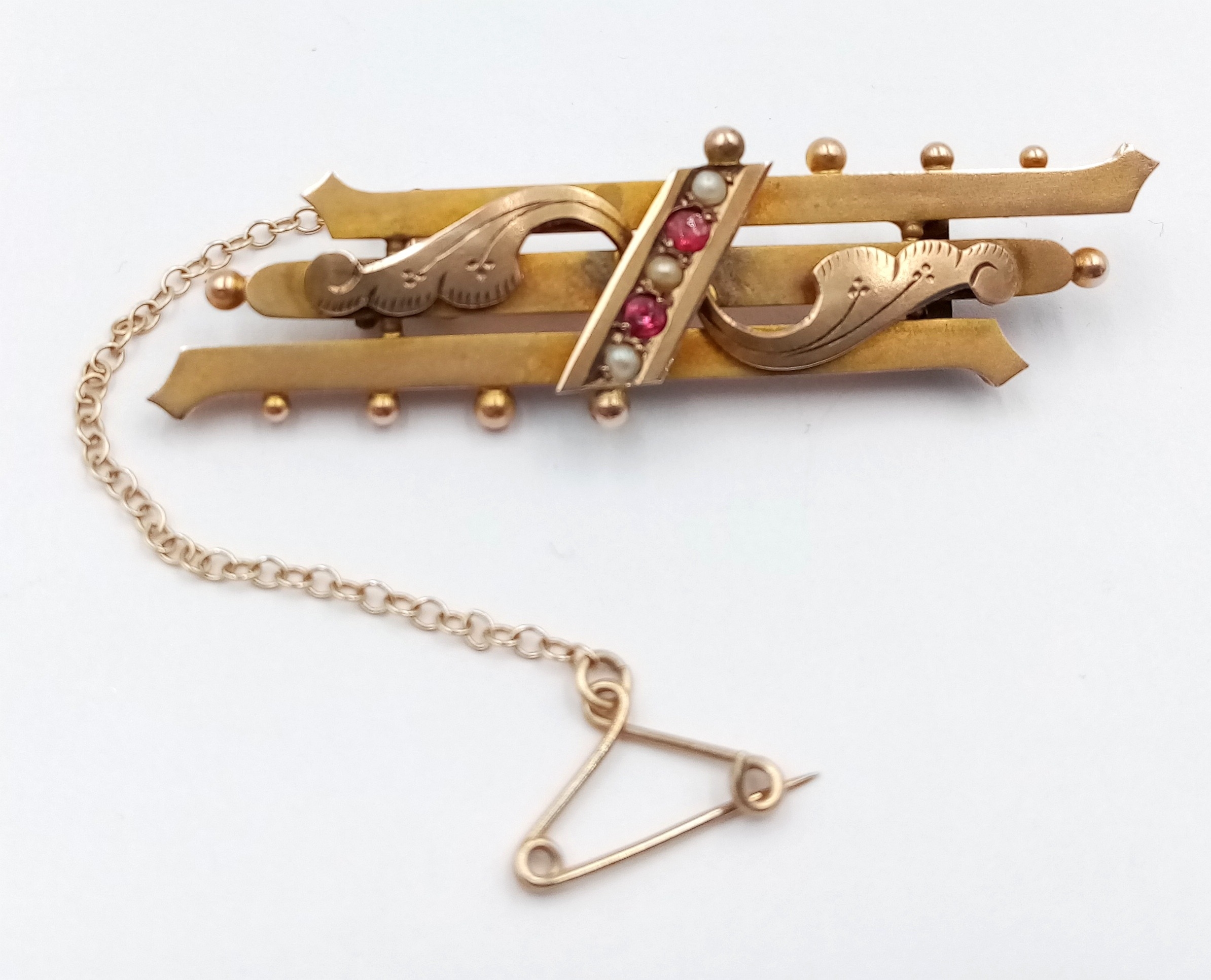 A vintage, 9 K yellow gold brooch with rubies and seed pearls and a safety chain with pin. Length: