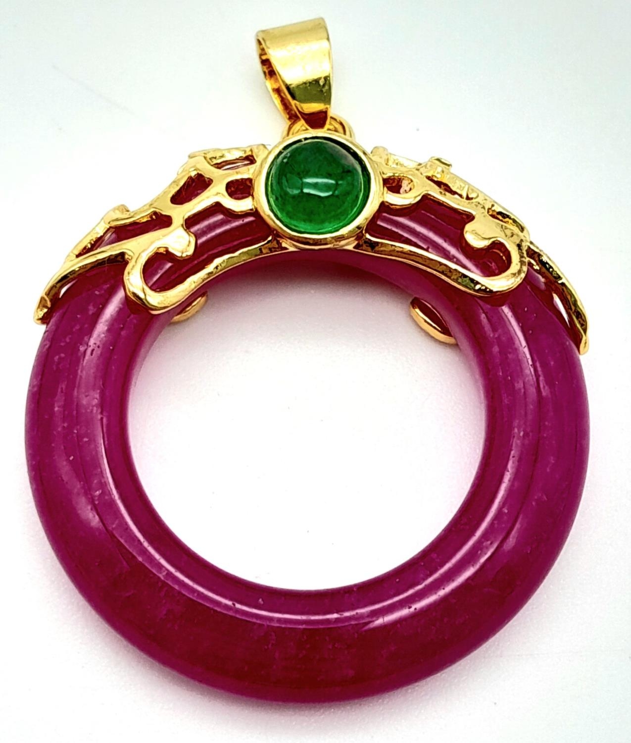 A Magenta Jade Pendant on Gilded Backing. 4cm length, 3cm diameter, 6.79g total weight.