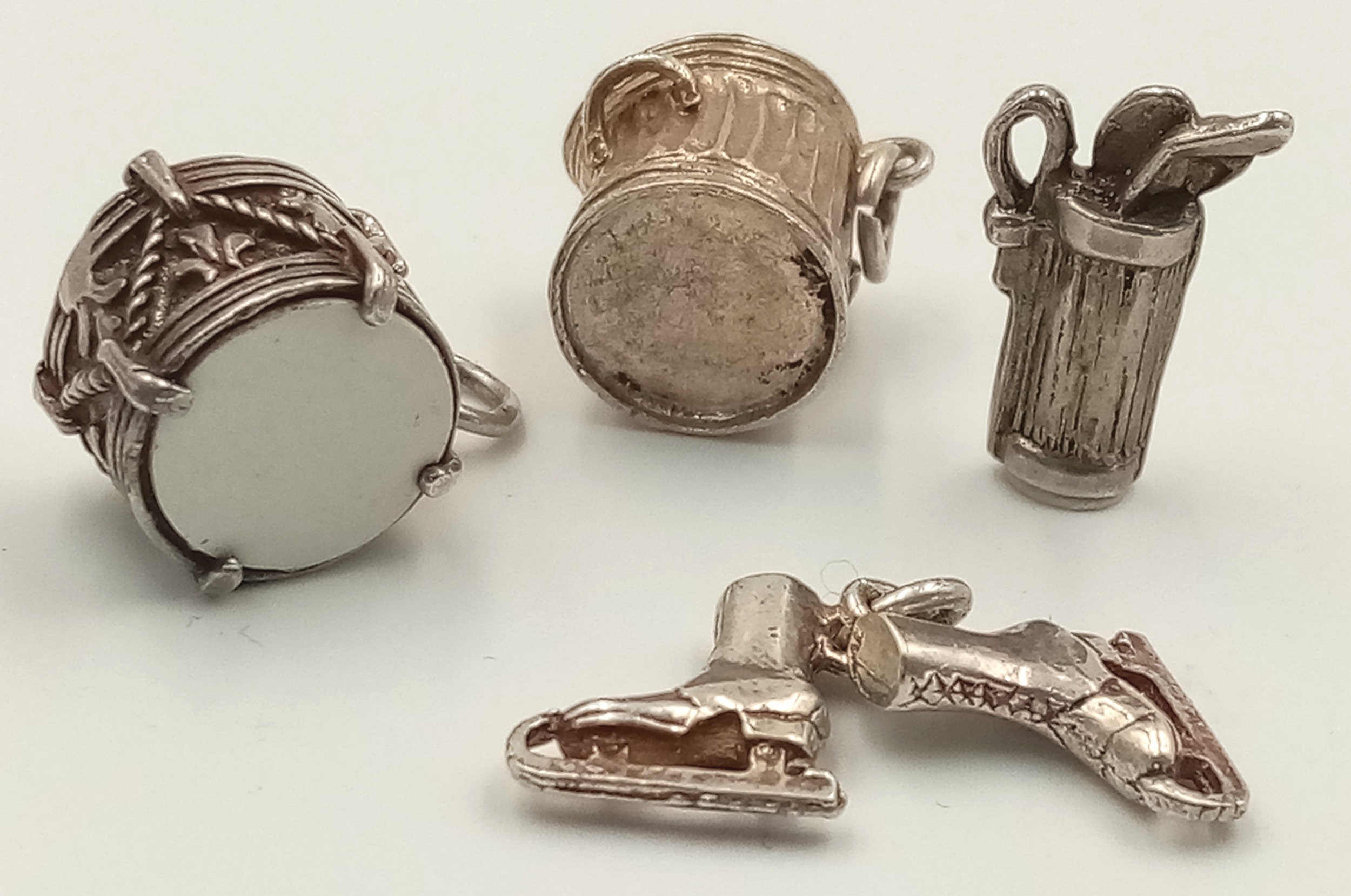 A SELECTION OF 4 X STERLING SILVER CHARMS - DUSTBIN, ICE SKATES, GOLF BAG WITH CLUBS, AND DRUM. 9g