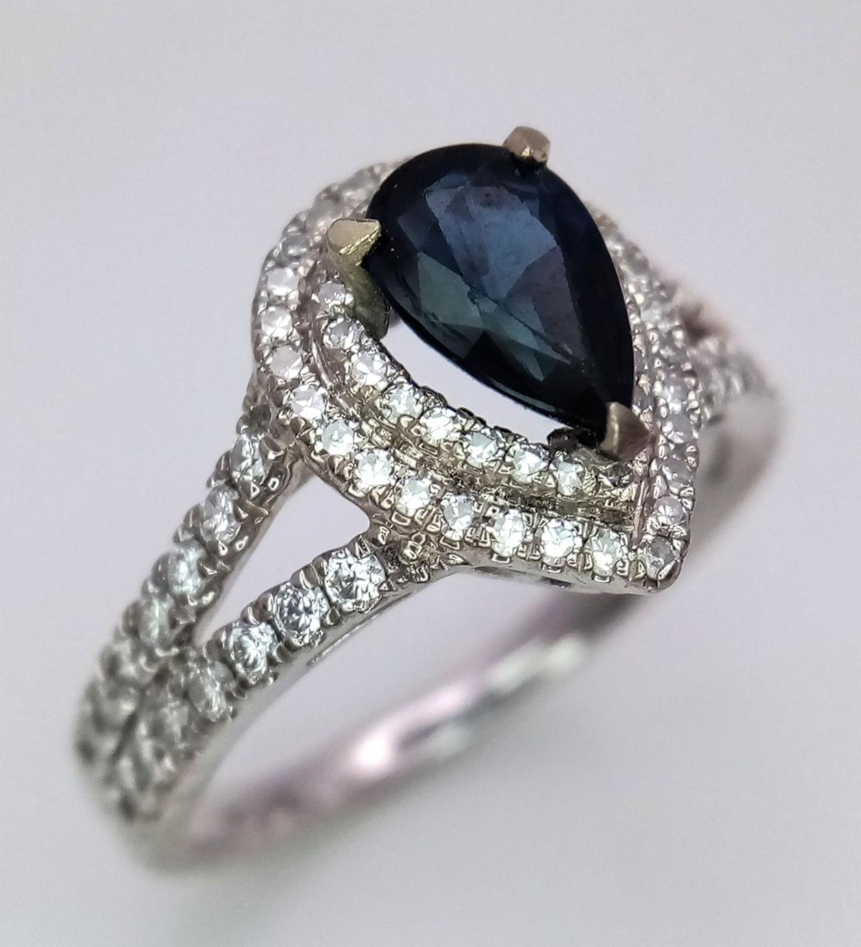 An 18K White Gold Sapphire and Diamond Ring. Teardrop sapphire with a 0.50ctw diamond surround. Size