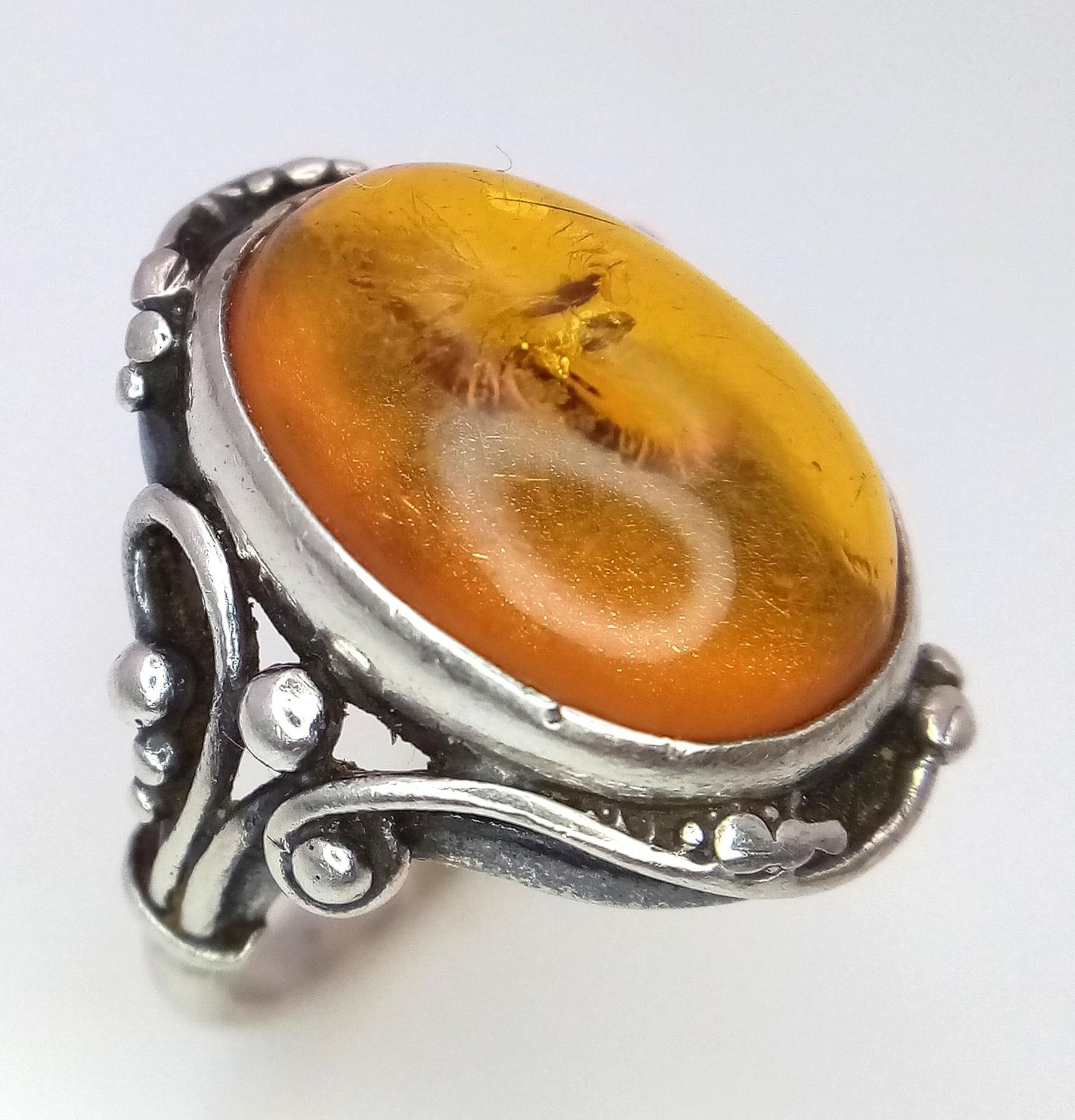 A Vintage or Antique, Ornate Mounted, Silver Amber Cabochon Ring Size S. Set with a 1.8cm Long Amber