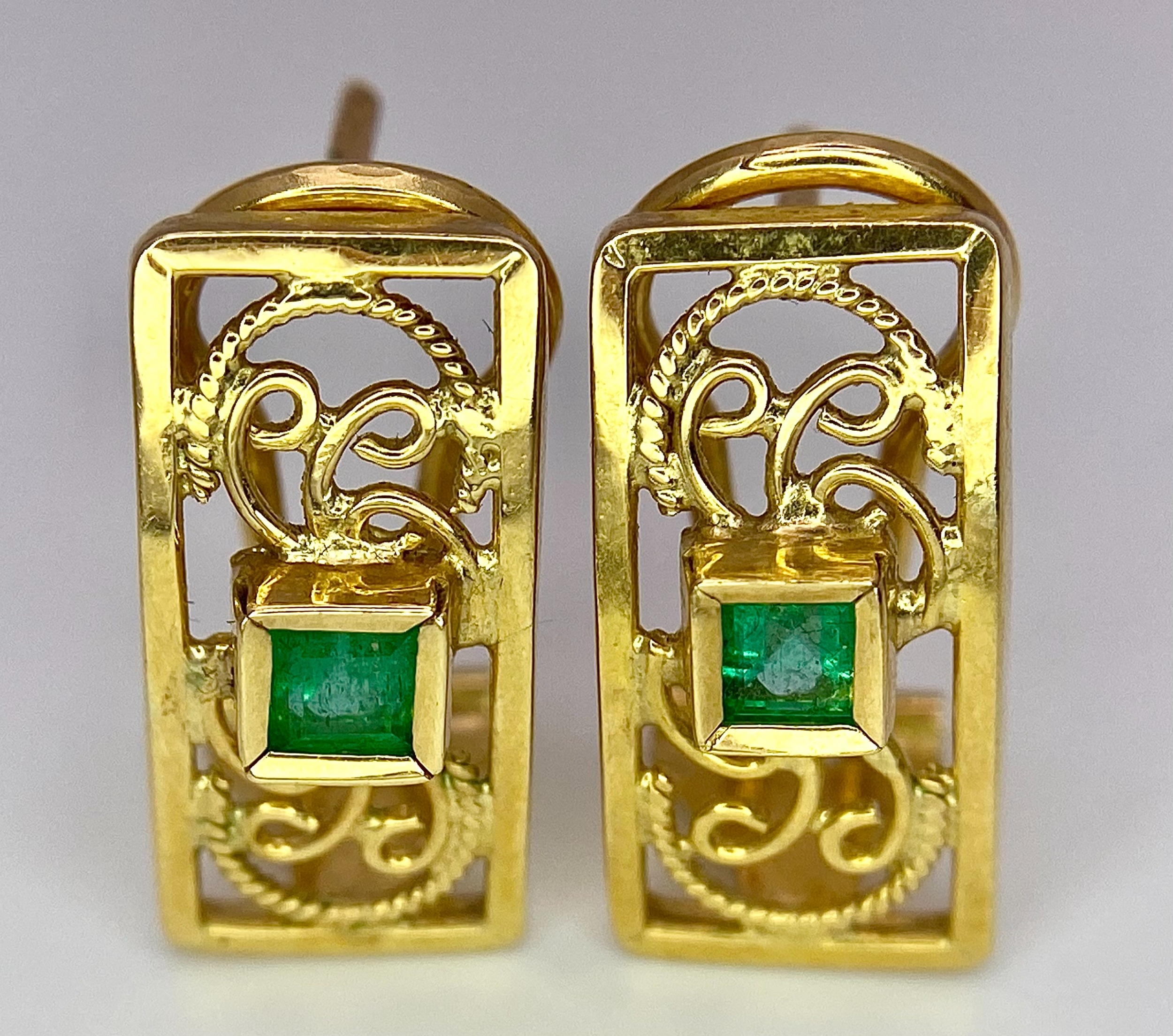 A Pair of 18K Yellow Gold and Emerald Earrings. Clip clasp with pierced decoration. 17mm. 3.9g total