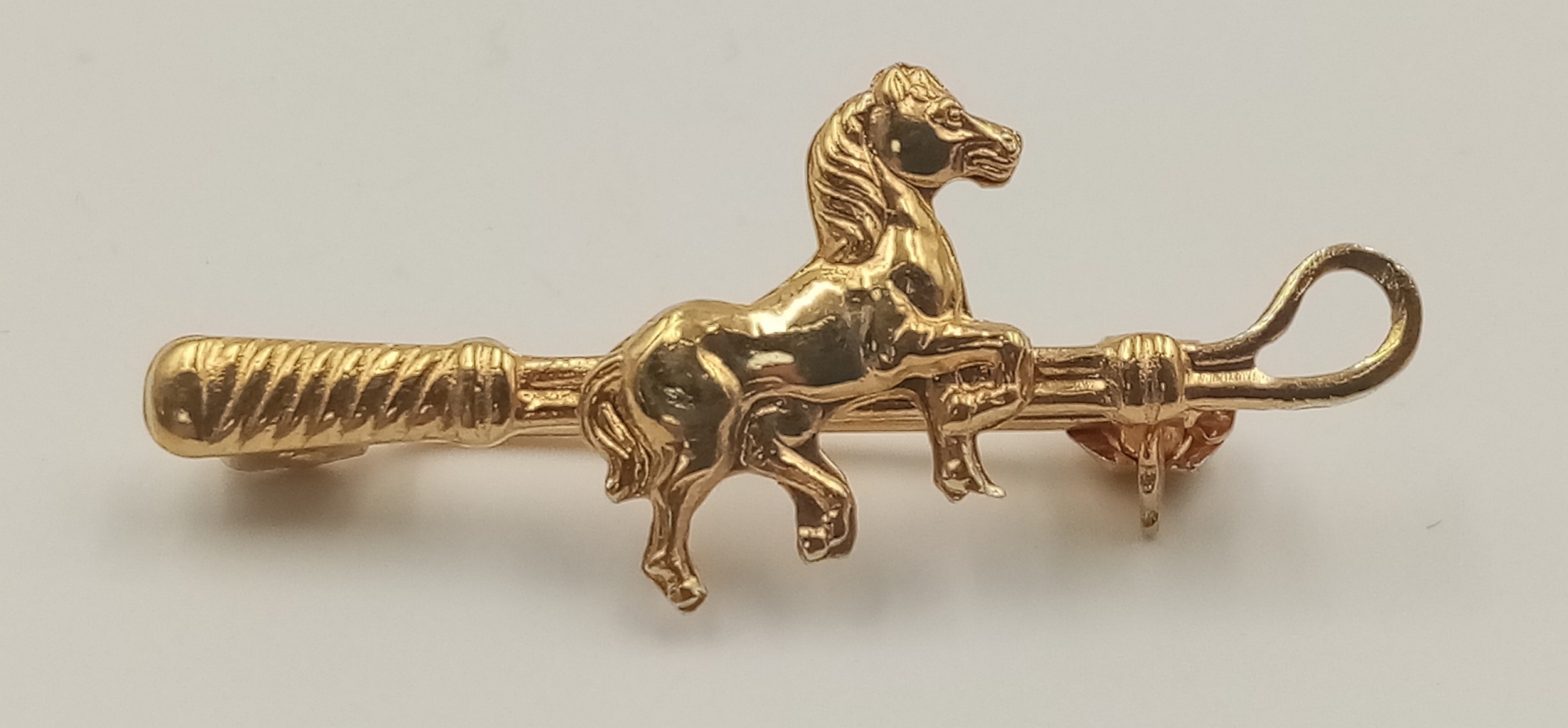 An 18 K yellow gold of riding interest depicting a horse and a riding crop, pin in excellent