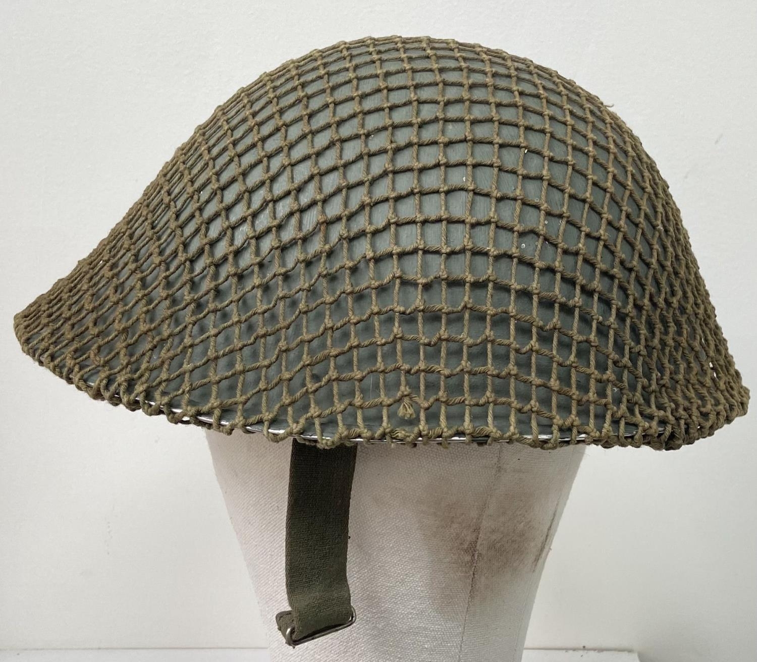 A British Army Mark V steel helmet, complete with camouflage net. Very good condition