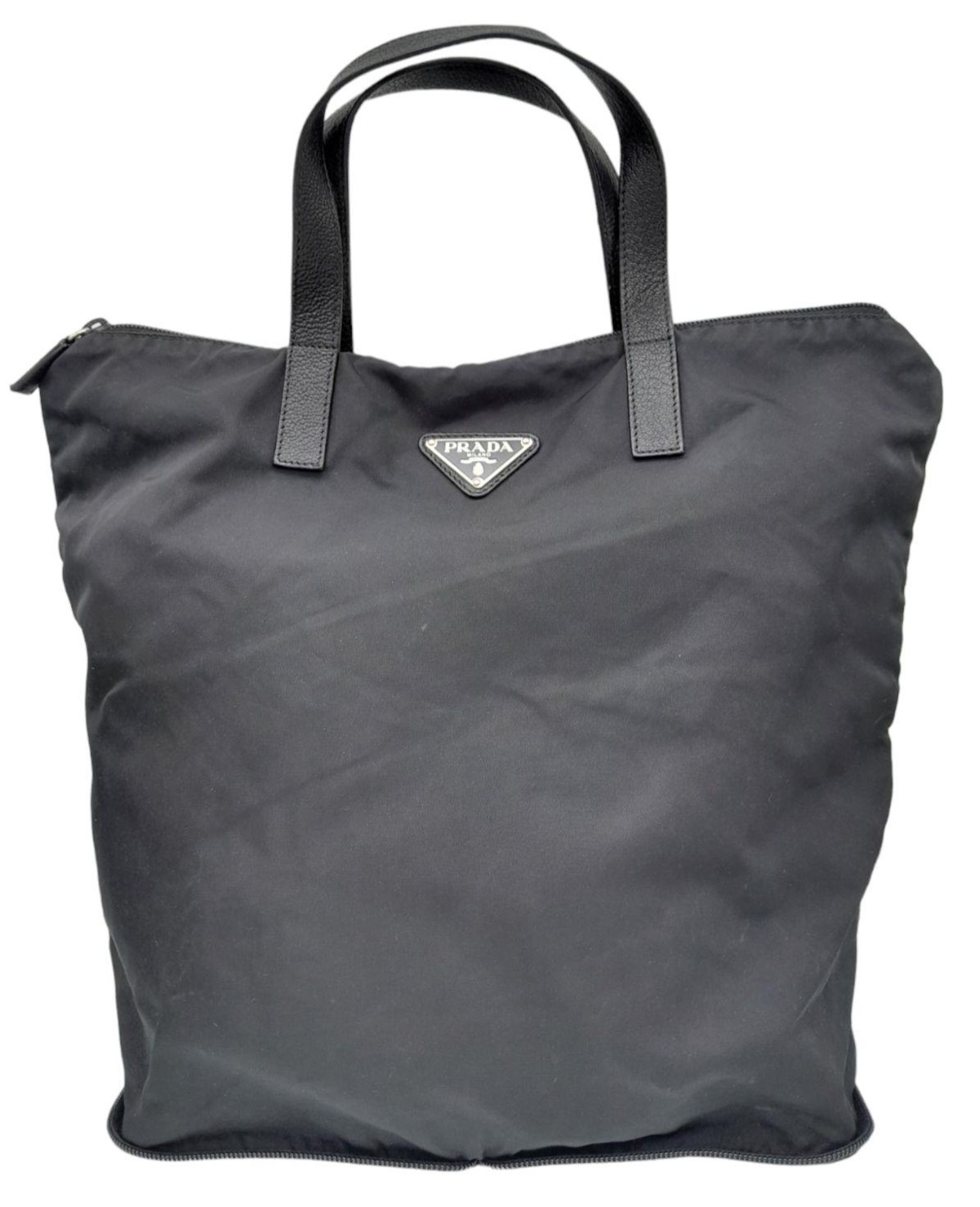 A Prada Black Compactable Tote Bag. Textile exterior with leather handles and zip top closure. Black