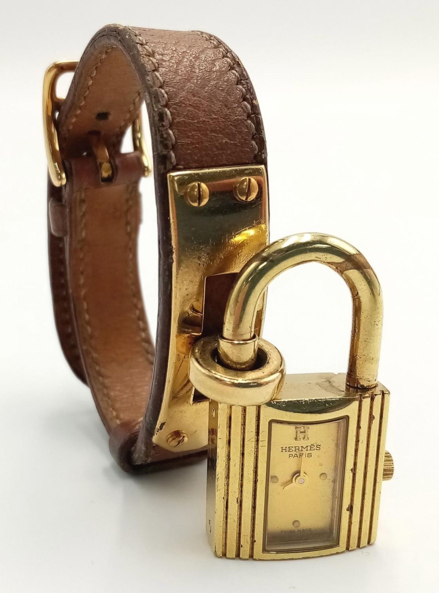 A Hermes Kelly Watch. Brown leather strap. Gold plated padlock quartz watch. Needs a battery so as