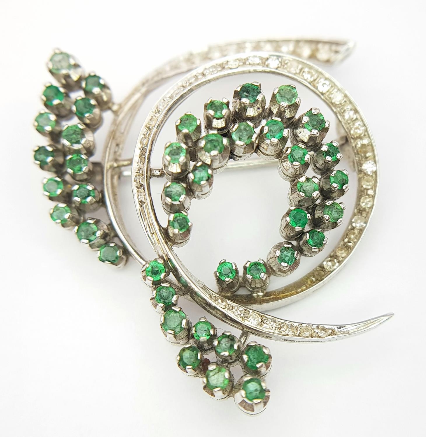 A Beautiful 18K White Gold Emerald and Diamond Swirling Brooch. 2ctw of round cut emeralds and