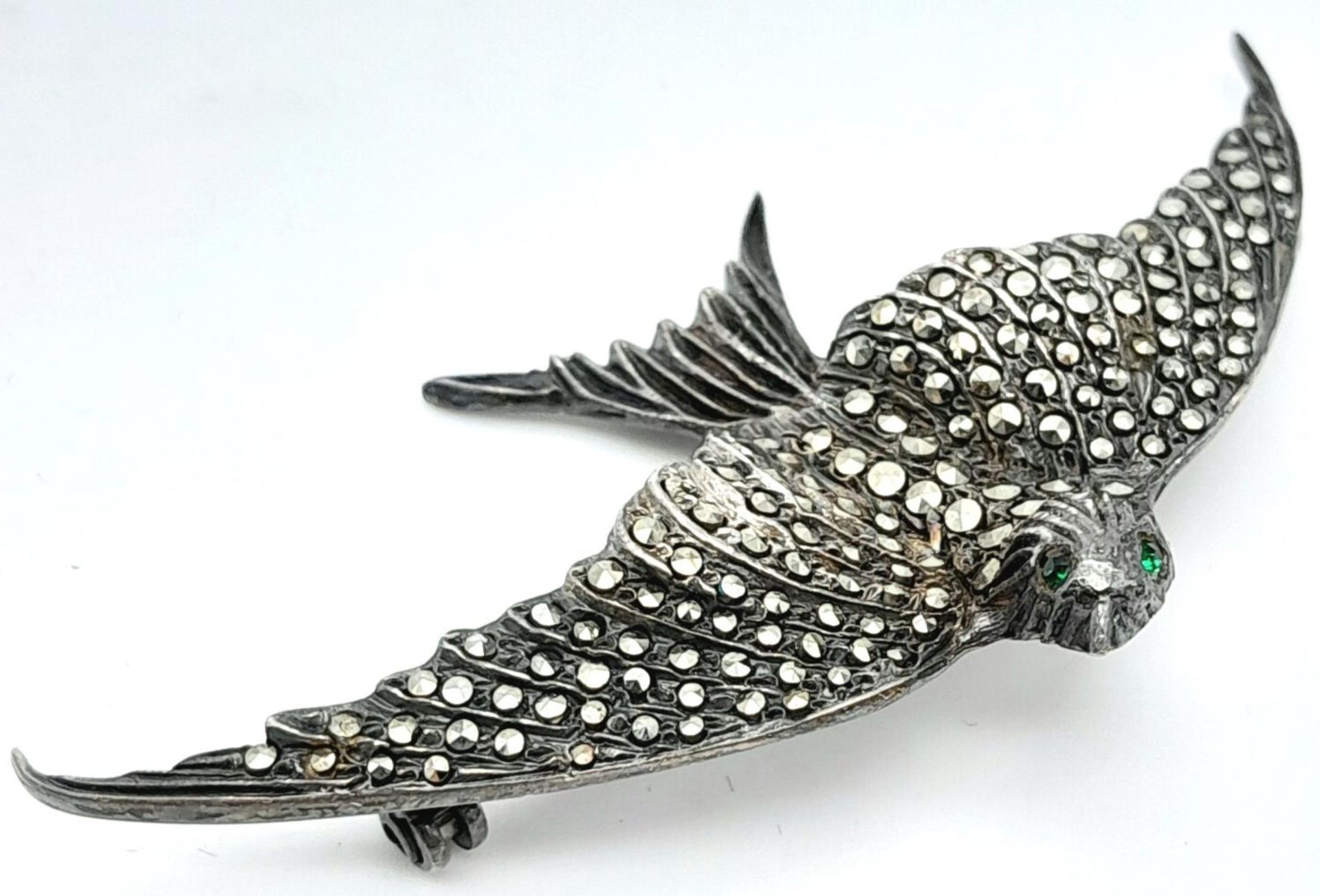 A Vintage Silver and Marcasite Brooch of a Bird in Flight. 7cm wingspan. Green stone eyes.