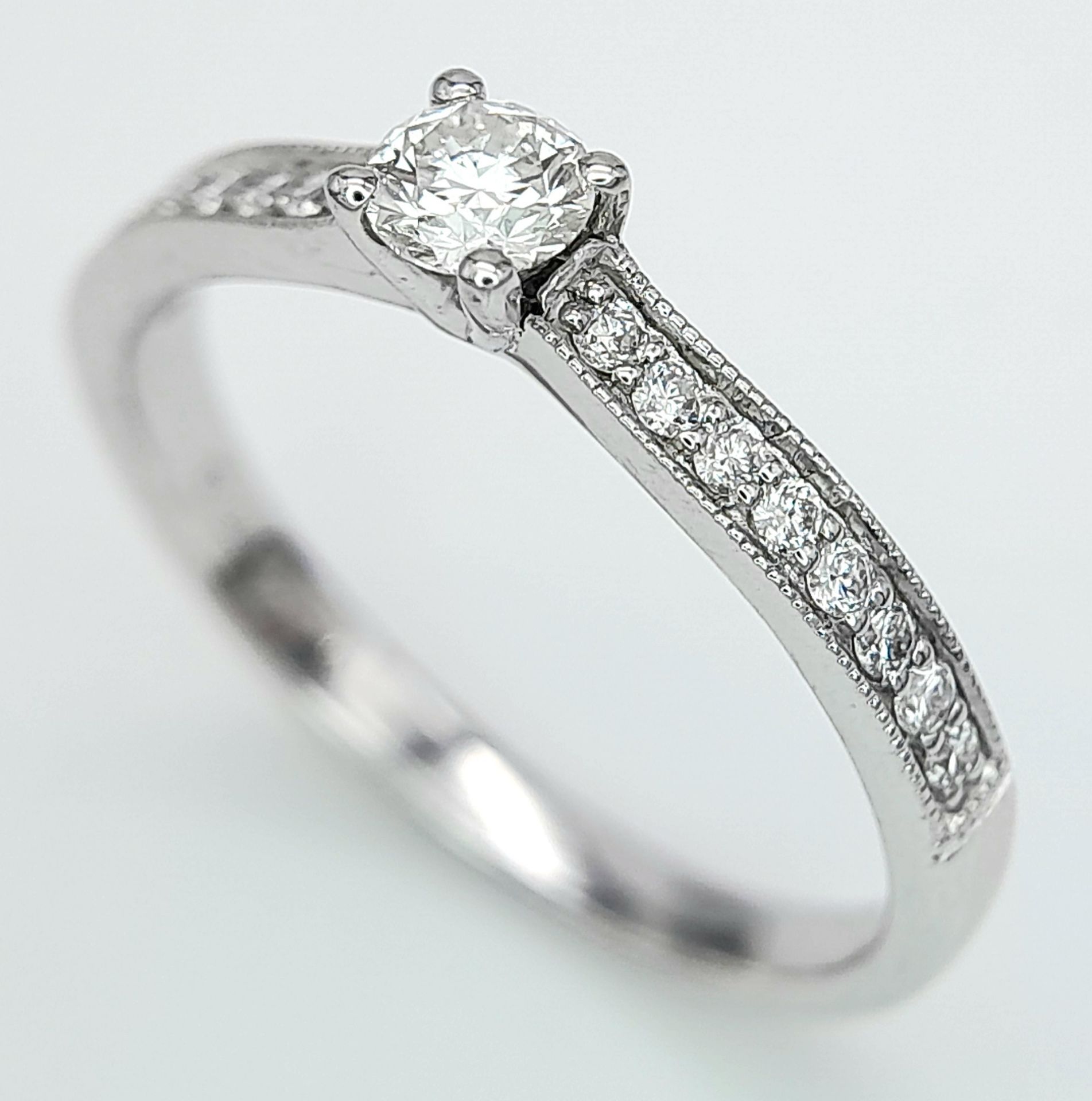 AN 18K WHITE GOLD DIAMOND SOLITAIRE RING - WITH DIAMOND SET SHOULDERS. 0.35CT. TOTAL 2.6G. SIZE N