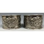 A pair of Chinese silver coloured metal napkin rings, decorated dragons chasing a flaming pearl (
