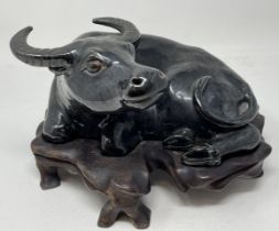 A Chinese pottery figure, of a recumbent water buffalo, on a hardwood stand, 17 cm high, and two
