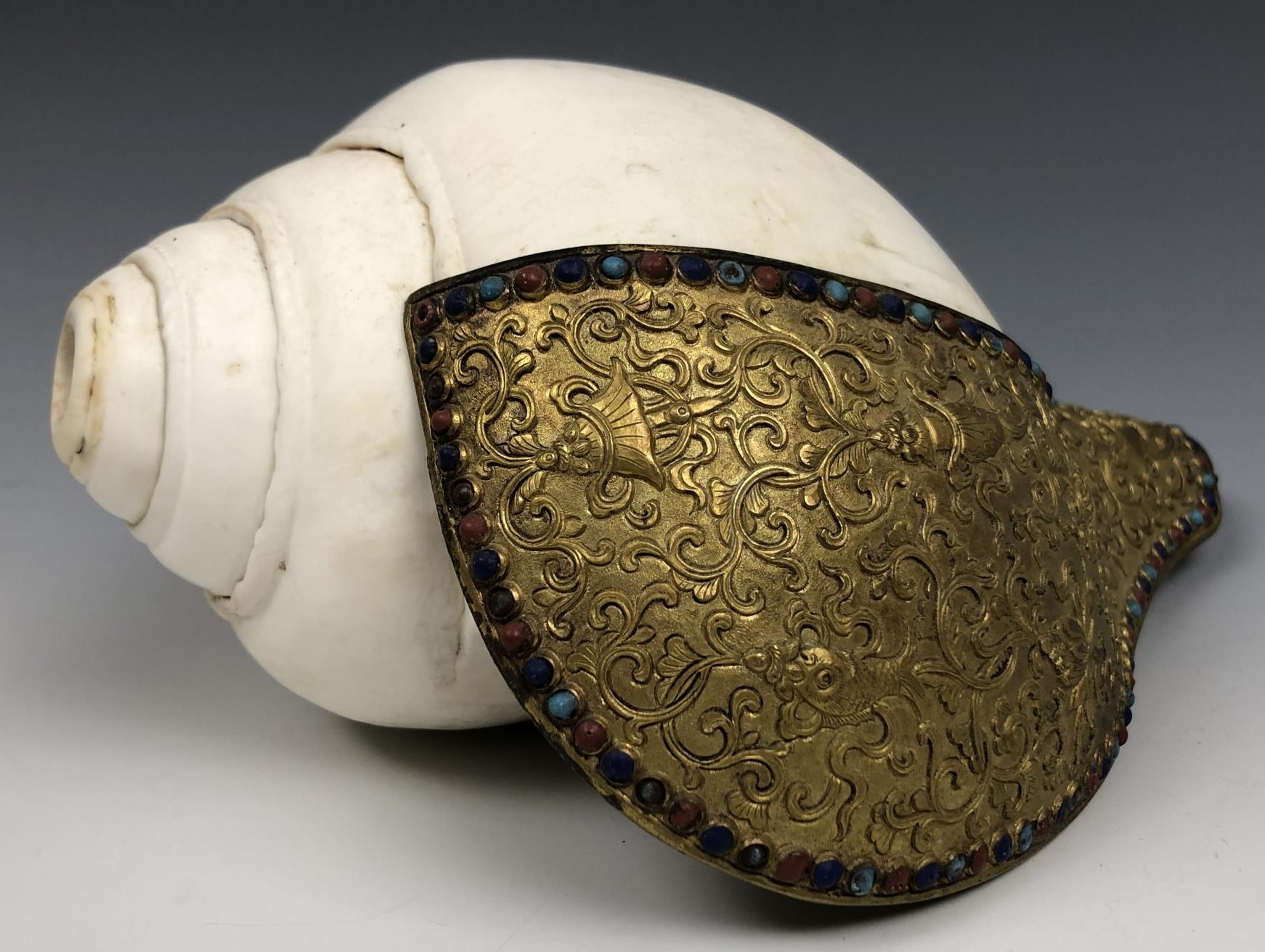 A Chinese conch shell trumpet, with a gilt bronze flange decorated in relief, with the eight