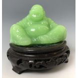 A Chinese green Buddha, 7 cm high, on an associated carved wooden base probably glass, not hardstone