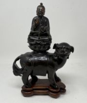 A Chinese bronze group, of a Buddha seated atop a Shi Shi dog, 26 cm high, on a hardwood stand There