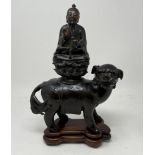 A Chinese bronze group, of a Buddha seated atop a Shi Shi dog, 26 cm high, on a hardwood stand There