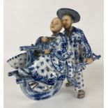 A Dutch porcelain group of an Eastern man pushing a lady in a cart, 20 cm high, and a plate (2)