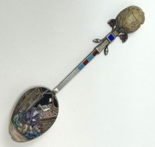 A silver coloured metal and enamel teaspoon, decorated in the Egyptian manner, the finial inlaid