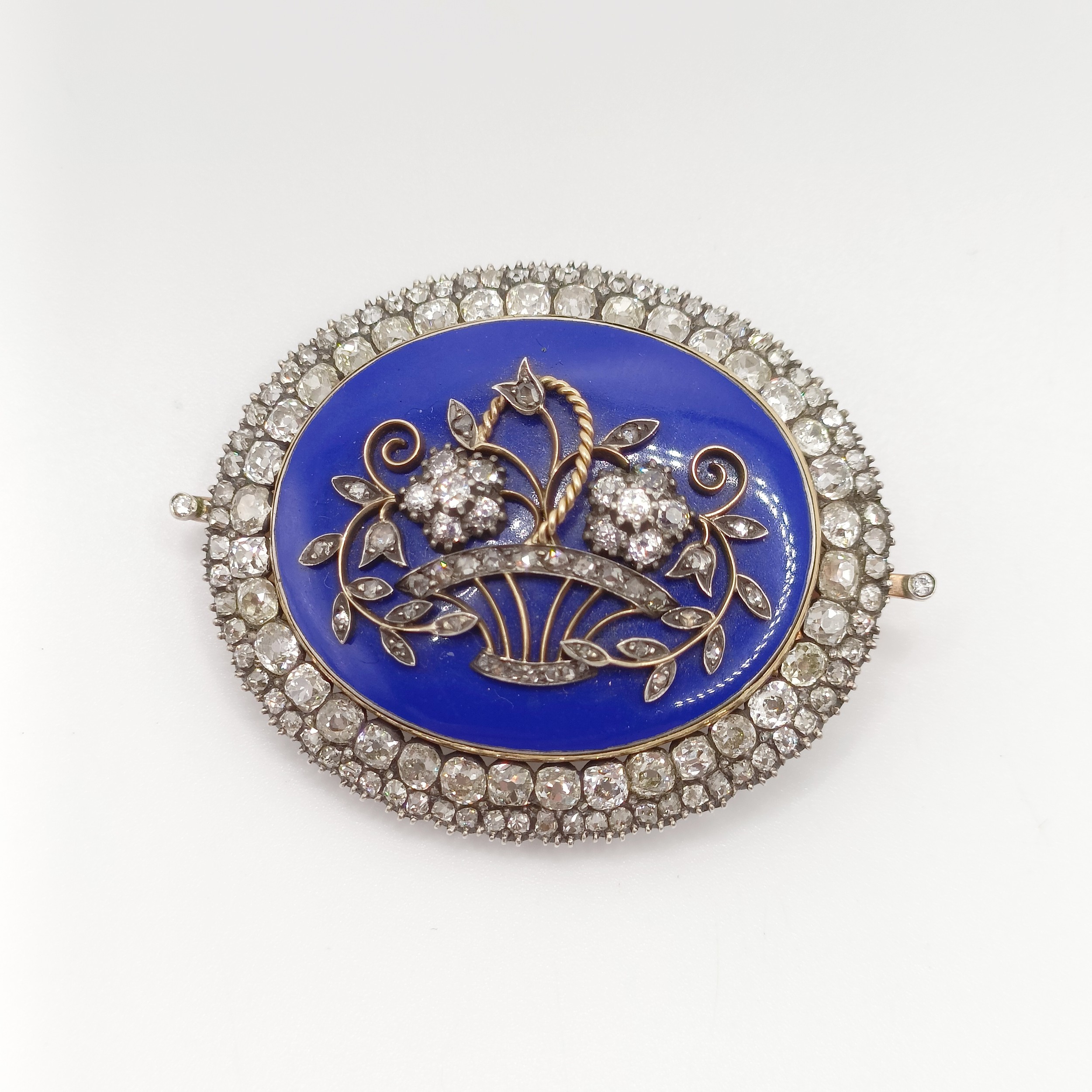 An early 19th French diamond, blue enamel, yellow and white metal oval brooch, decorated a basket of