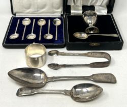 A fiddle pattern spoon, another, a napkin ring, a pair of sugar tongs, an egg cup and spoon,
