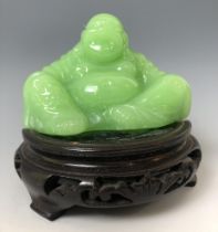 A Chinese green Buddha, 7 cm high, on an associated carved wooden base probably glass, not hardstone