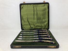 A set of six 19th century knives, with porcelain pistol handles, and silver sheaths, cased