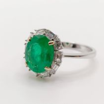 An 18ct white gold ring, set with an oval emerald and surrounded by baguette cut diamonds, emerald