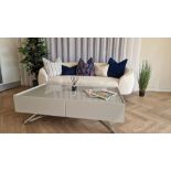 CREAM COLOURED FABRIC TWO SEATED SOFA WITH FIVE VARIOUS CUSHIONS. GLOSS GREY TWO DRAWER COFFEE TABLE