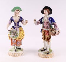 A pair of porcelain figures depicting a young man carrying a basket of fruit and a young woman