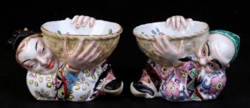 A pair of continental Chinese style salts in the form of wise men holding bowls, each 9cms