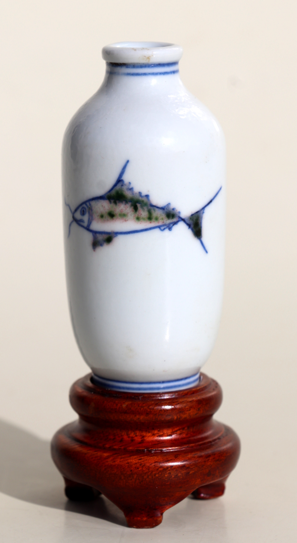 A Chinese porcelain snuff bottle decorated with fish, on a hardwood stand, 7.5cms high. Condition