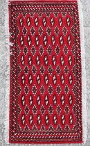 A small Persian Turkoman rug with repeat stylised design on a red ground, approx 130 by 60cms.