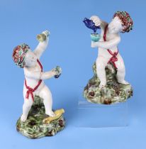 A pair of continental majolica figures depicting Putti with wine glasses wearing wreaths in their