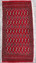 A small Persian Turkoman rug with repeat stylised design on a red ground, approx 130 by 60cms.