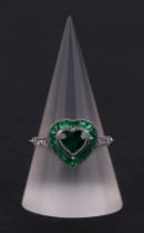 A platinum ring set with a heart shaped emerald, surround by calibre cut emeralds and diamond set