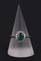An 18ct white gold oval emerald and diamond cluster ring, approx UK size N.