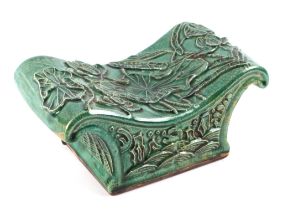 A Chinese green glazed pottery neck rest or pillow decorated in relief with lily pads, 23cm wide.