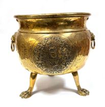 A 19th Centaury brass log bin, with lion mask handles and armorial crest, standing on three lion paw