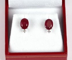 A pair of platinum stud earrings set with oval cut treated rubies and a single diamond, rubies