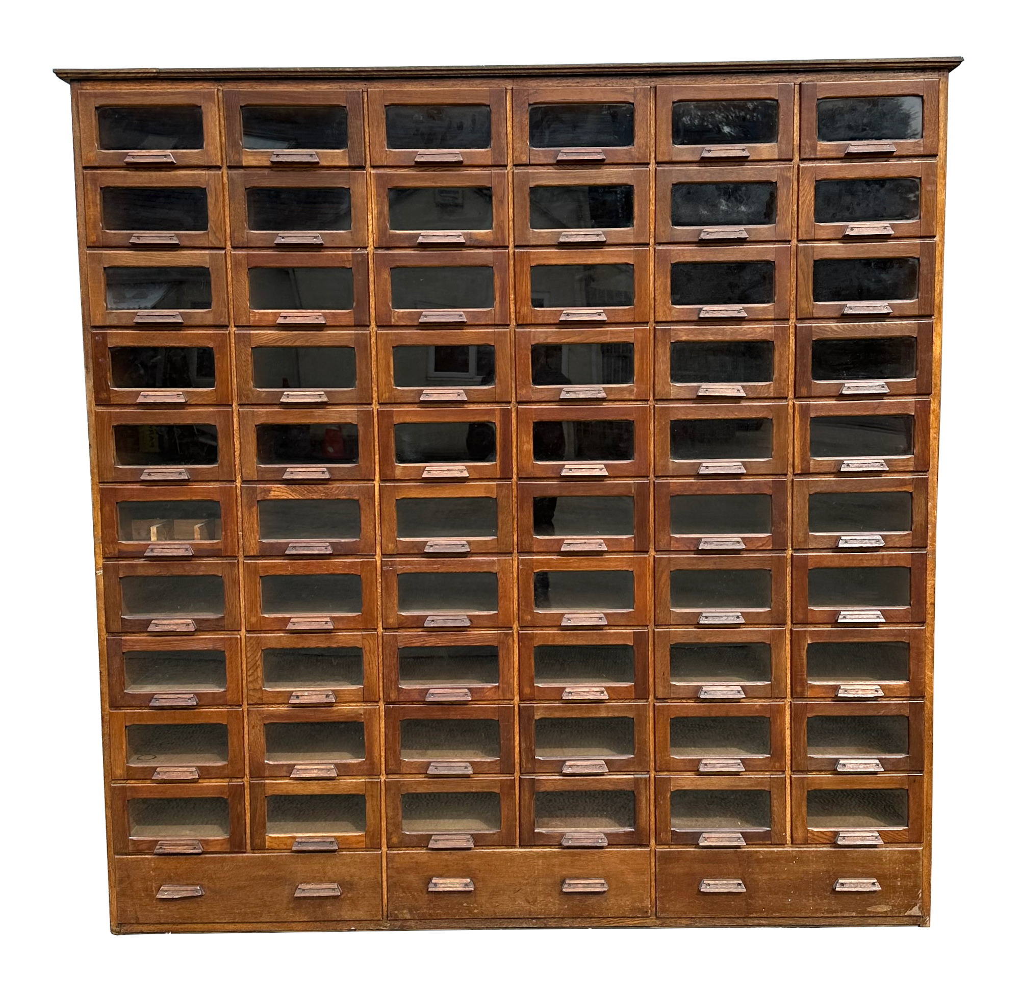 A mid century substantial haberdashery cabinet, with sixty oak fronted glazed drawers, above three