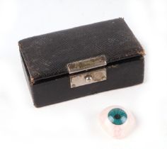 A prosthetic glass eye, in a tooled leather suede lined box.