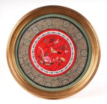 A Chinese embroidered silk work panel, depicting a bird with flowers, 28cm diameter, framed and